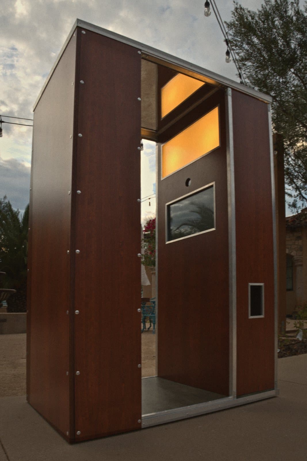 Le Booth photo booth at dusk with its panels lit from inside, string lights overhead
